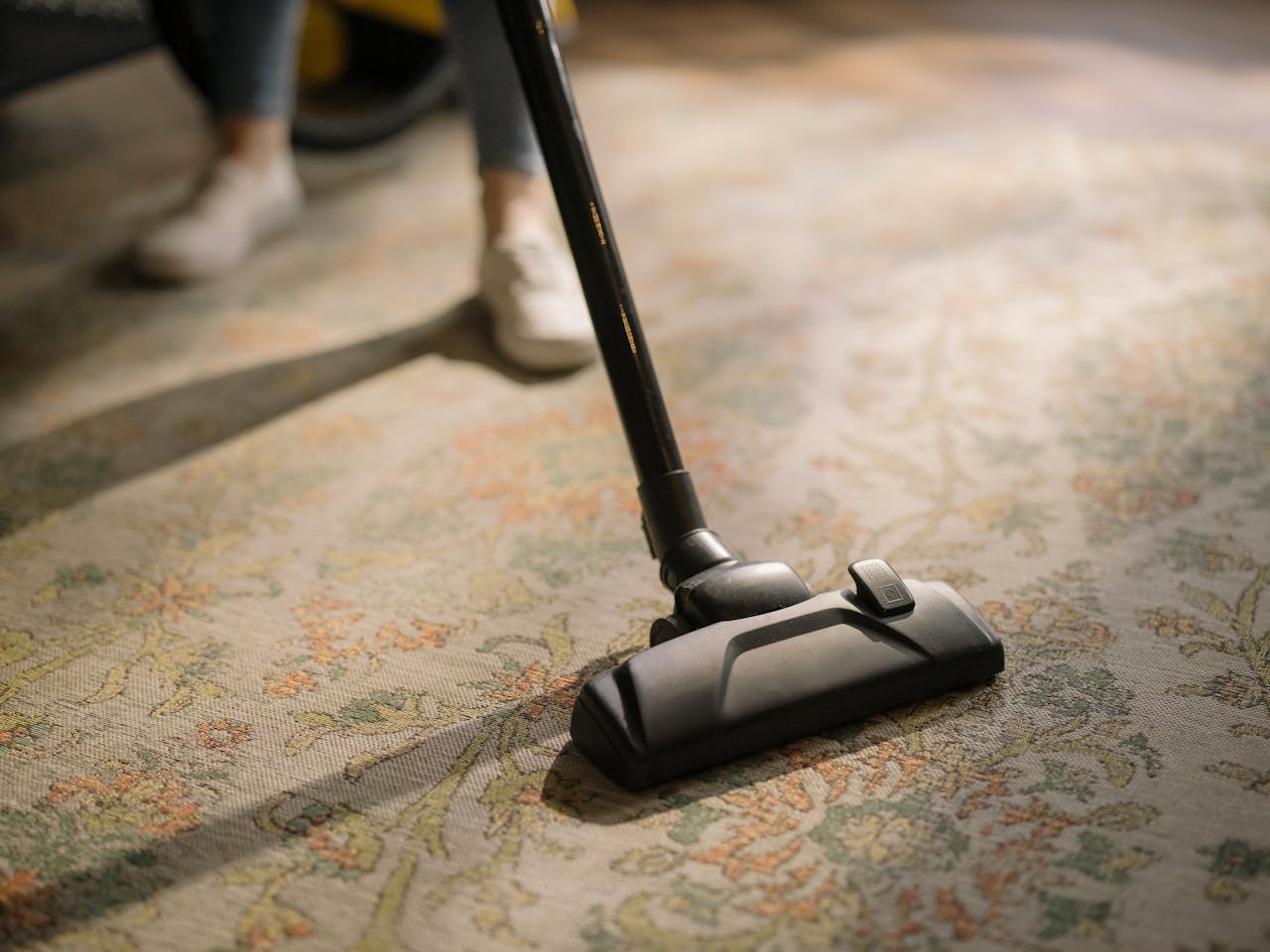 gallery-05 Close-up of a vacuum cleaner on a patterned carpet in a sunlit room, capturing a moment of household cleaning.